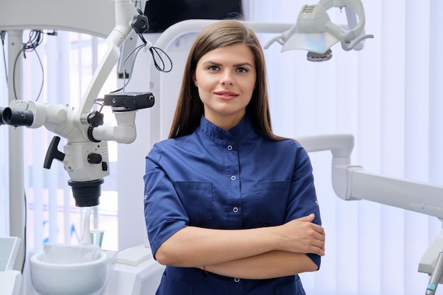 Portrait de jeune femme médecin dentiste confiante avec les mains jointes en cabinet dentaire. Concept de médecine, de dentisterie et de soins de santé