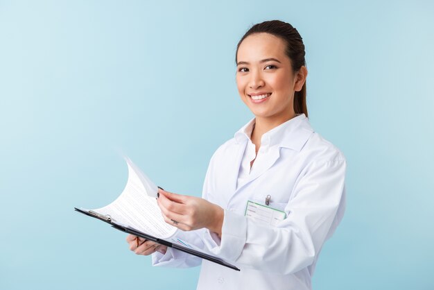 portrait d'une jeune femme médecin joyeuse posant isolé sur mur bleu tenant le presse-papiers.