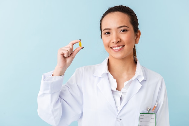 portrait d'une jeune femme médecin posant isolé sur mur bleu tenant des pilules.