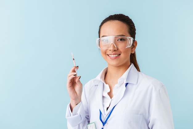 portrait d'une jeune femme médecin posant isolé sur mur bleu tenant la seringue.