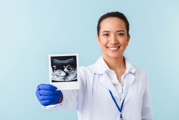 portrait d'une jeune femme médecin posant isolé sur mur bleu tenant x-ray de bébé dans les mains.