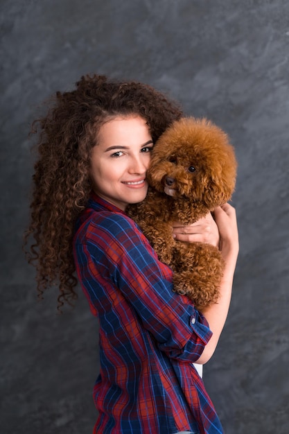 Portrait de jeune femme et mignon petit chien sur fond gris studio. Chiot caniche toy dans les mains des femmes, espace copie