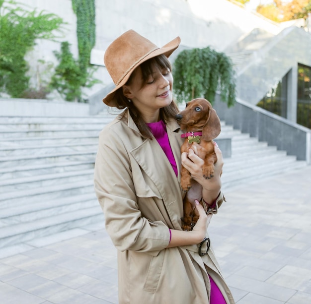 Portrait d'une jeune femme à la mode et d'un adorable chiot teckel dans un parc de la ville. Maîtresse et animal de compagnie