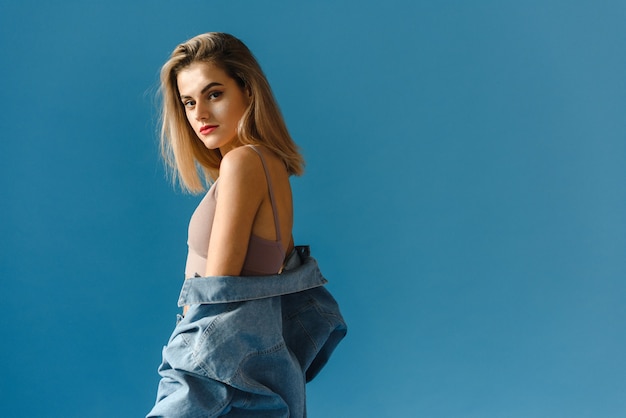 Portrait d'une jeune femme à la mode dans une veste en jean et un jean sur fond bleu.