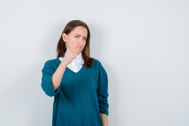 Portrait de jeune femme montrant le geste du gagnant en pull sur chemise blanche et à la vue de face confiant