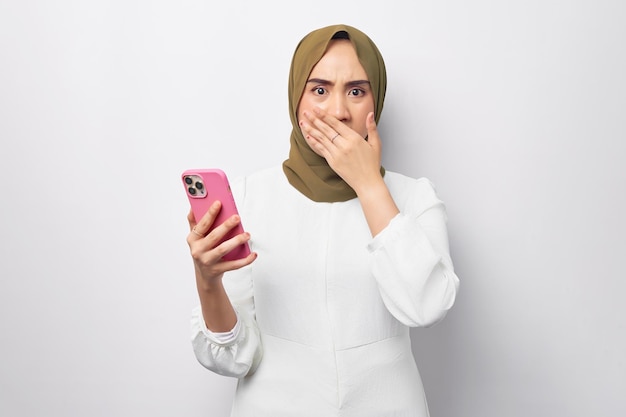 Portrait d'une jeune femme musulmane asiatique arabe surprise portant le hijab vert tenant un téléphone portable et couvrant la bouche avec la main isolée sur fond blanc Concept de style de vie religieux des gens