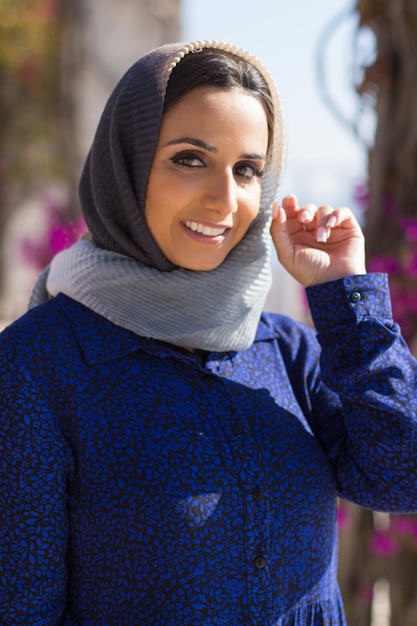 Photo portrait de jeune femme musulmane souriante. belle femme en foulard gris debout calmement à l'extérieur pendant la journée avec la main près de son visage. concept de beauté et d'ethnicité