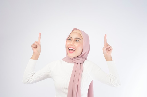 Un portrait de jeune femme musulmane souriante portant un hijab rose sur blanc.