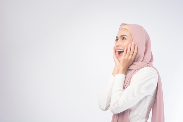 Un portrait de jeune femme musulmane souriante portant un hijab rose sur blanc.