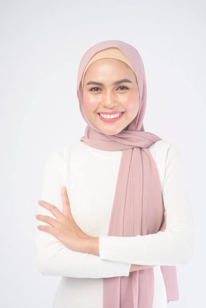 Un portrait de jeune femme musulmane souriante portant un hijab rose sur blanc.