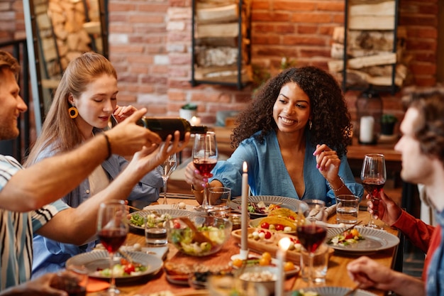 Portrait de jeune femme noire appréciant un verre de vin lors d'un dîner avec des amis dans un chaleureux s