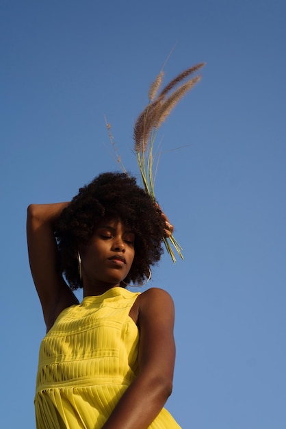 Portrait d'une jeune femme noire portant une robe jaune tenant de l'herbe