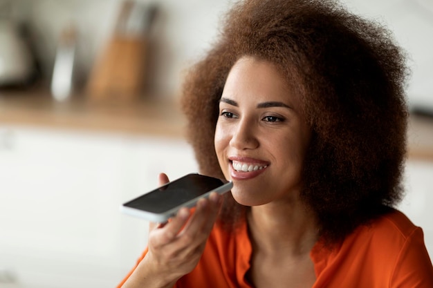 Portrait d'une jeune femme noire souriante enregistrant un message vocal sur un smartphone