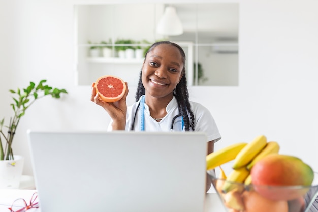 Portrait de jeune femme nutritionniste souriante dans la salle de consultation. Bureau de nutritionniste avec fruits sains, jus et ruban à mesurer. Diététicien travaillant sur le plan de régime.