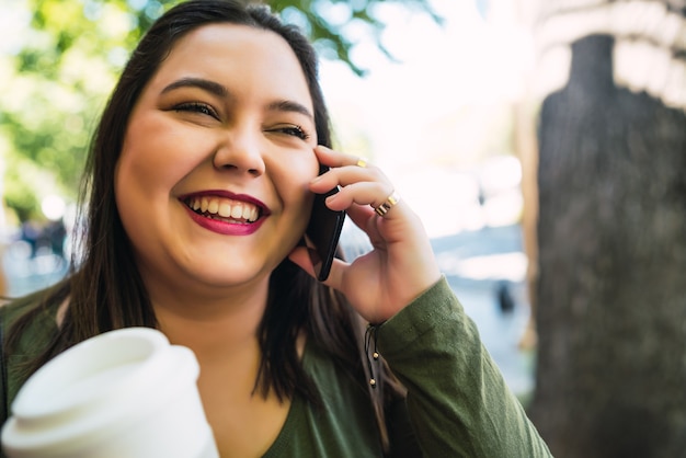 Portrait de jeune femme parlant au téléphone tout en tenant une tasse de café à l'extérieur dans la rue
