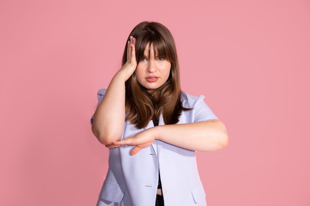 Portrait d'une jeune femme pensant, ayant l'air fatiguée et ennuyée par des problèmes de dépression avec le bras près d'entendre, prise de vue en studio, fond rose.