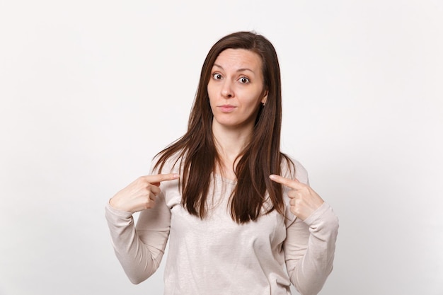 Portrait d'une jeune femme perplexe et perplexe dans des vêtements légers pointant l'index sur elle-même isolé sur fond de mur blanc en studio. Concept de mode de vie des émotions sincères des gens. Maquette de l'espace de copie.