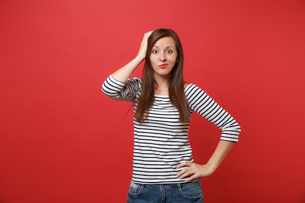 Portrait d'une jeune femme perplexe en vêtements rayés debout et mettant la main sur la tête