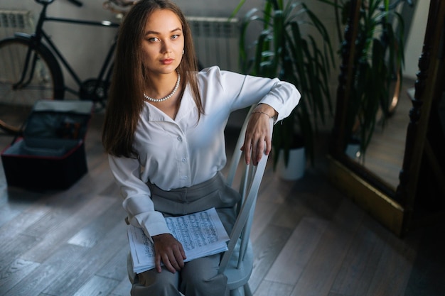 Portrait d'une jeune femme pianiste sérieuse tenant dans les mains une partition avec des notes de musique dans une salle de classe sombre regardant la caméra