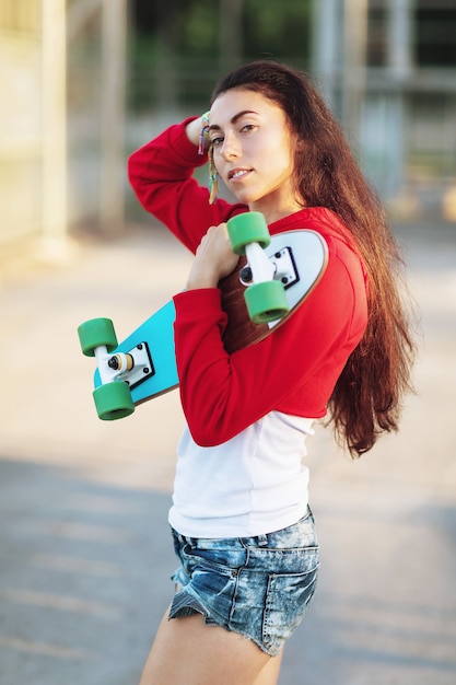 Portrait d'une jeune femme avec une planche à roulettes dans ses mains sur une soirée ensoleillée d'été