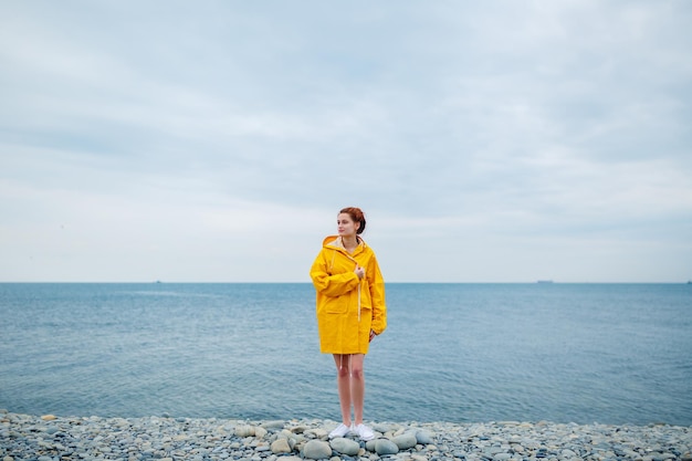 Portrait de jeune femme portant un imperméable jaune vif sur fond d'océan