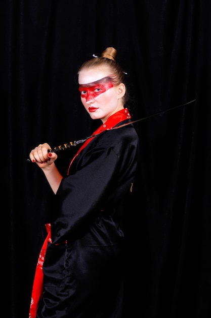 Photo portrait d'une jeune femme portant un kimono et un maquillage tenant une épée sur un fond noir