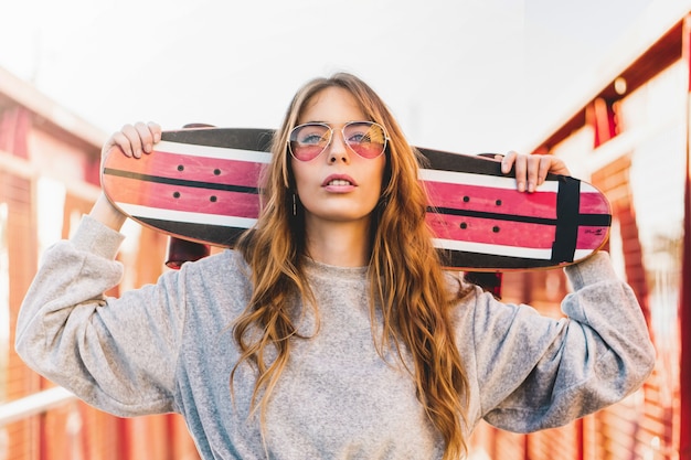 Portrait d'une jeune femme portant des lunettes rouges et tenant un long skateboard