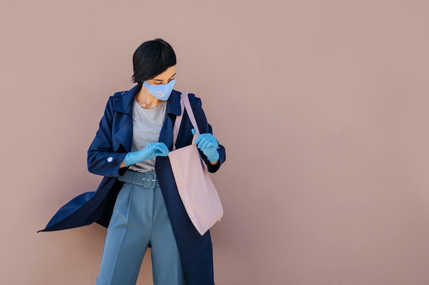 Portrait d'une jeune femme portant un masque en coton et des gants médicaux avec un sac à provisions dans la rue pendant l'épidémie de Covid 19. Protection en prévention contre le coronavirus.