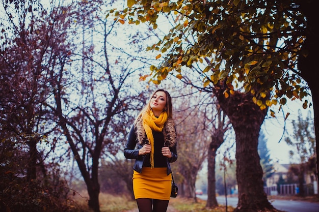 Portrait de jeune femme portant une veste en cuir noire et une écharpe jaune à l'extérieur