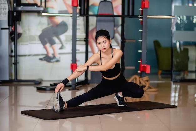 Portrait jeune femme portant des vêtements de sport et une montre intelligente assise sur le sol et étirant ses jambes et ses bras avant l'entraînement à la salle de fitness,