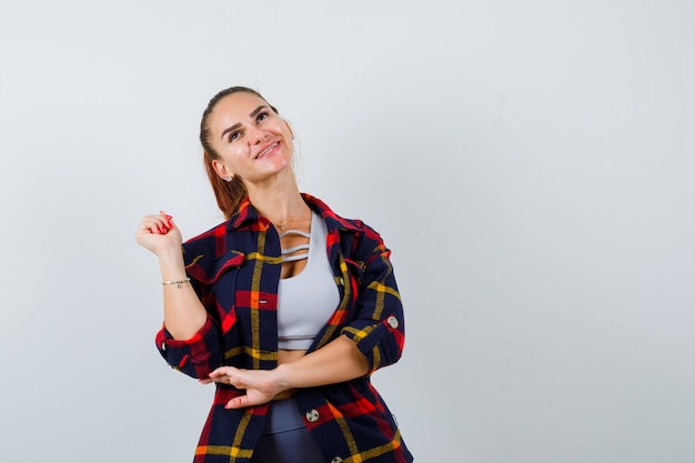 Portrait de jeune femme posant tout en regardant dans un haut court, une chemise à carreaux, un pantalon et à la vue de face heureuse