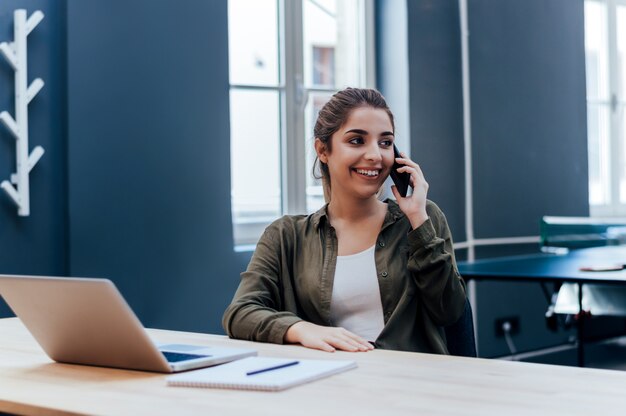 Portrait d&#39;une jeune femme prenant une conversation téléphonique, assis à une table à la maison.