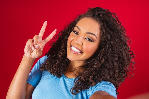 Portrait de jeune femme prenant selfie avec signe de la main de la paix. Femme afro faisant une photo de selfie avec signe v.