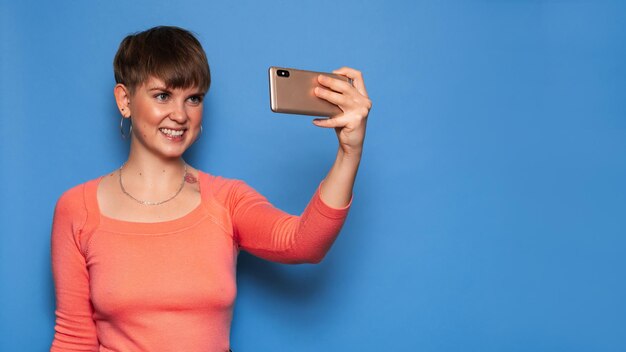 Portrait d'une jeune femme prenant un selfie sur un smartphone sur fond bleu. Une place pour votre texte. Le concept de communication vidéo à distance.