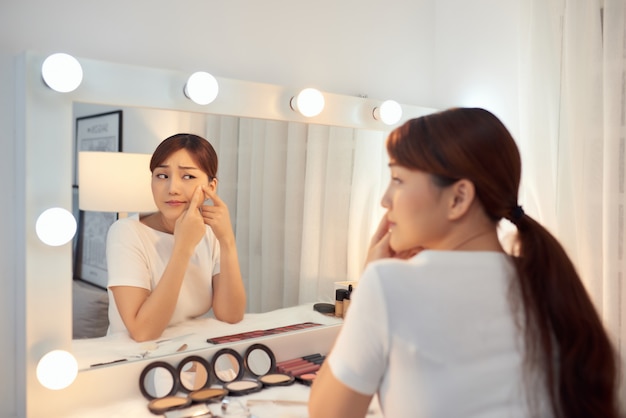 Portrait de jeune femme avec problème d'acné regardant dans un miroir