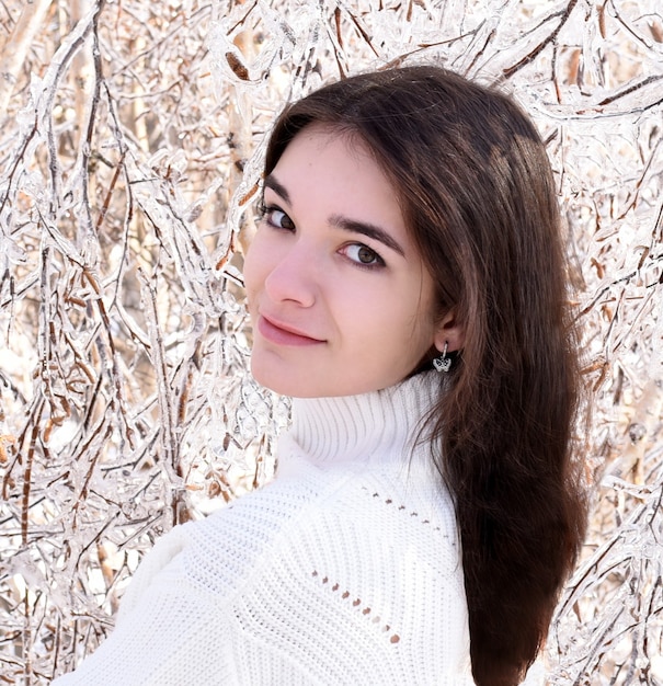 Portrait de jeune femme en pull à côté d'arbres gelés recouverts de glace