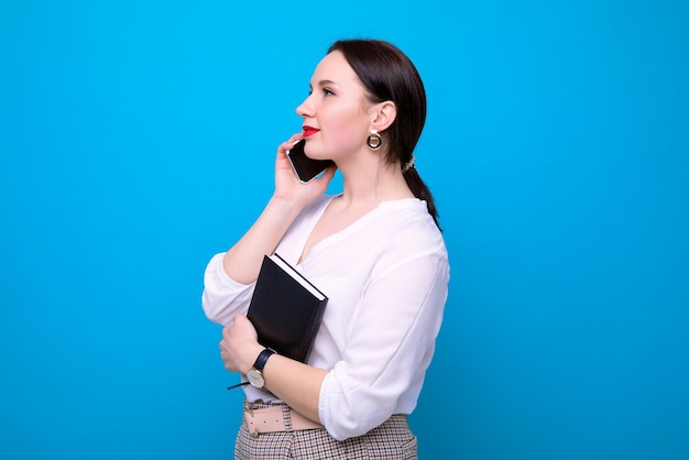 Portrait d'une jeune femme qui parle au téléphone tenant un cahier dans ses mains Processus d'affaires