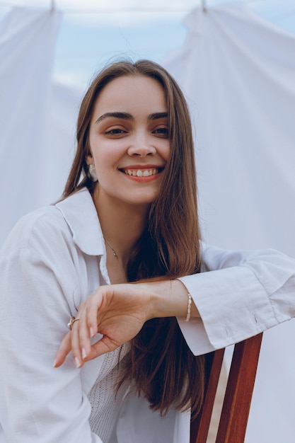 Portrait d'une jeune femme ravie aux cheveux bruns assise sur une chaise dans la nature et regardant la caméra