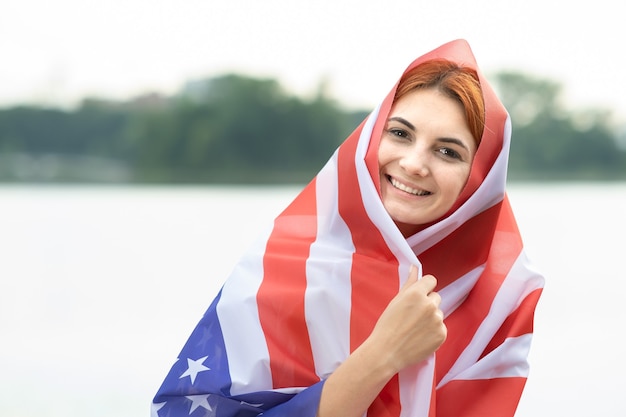 Portrait de jeune femme réfugiée heureuse avec drapeau national des USA sur sa tête et ses épaules