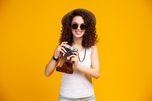 Portrait de jeune femme en riant à lunettes à prendre des photos sur un appareil photo vintage rétro isolé sur jaune vif