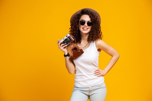 Portrait de jeune femme en riant à lunettes à prendre des photos sur un appareil photo vintage rétro isolé sur jaune vif