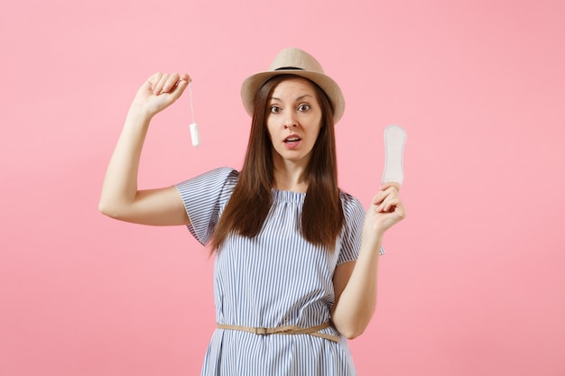 Portrait de jeune femme en robe bleue tenant une serviette hygiénique, tampon pour les jours de menstruation de sécurité variante isolés sur fond rose. Soins médicaux, gynécologique, concept de choix. Espace de copie.