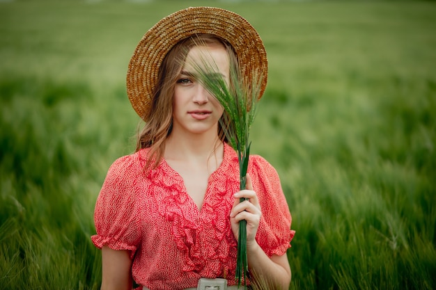 Portrait de jeune femme en robe et chapeau en champ vert d'orge en campagne