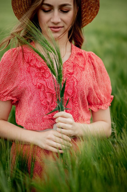 Portrait de jeune femme en robe et chapeau dans un champ vert d'orge dans la campagne Fille élégante en rustique profitant d'un moment paisible dans l'herbe en été Moment rural tranquille