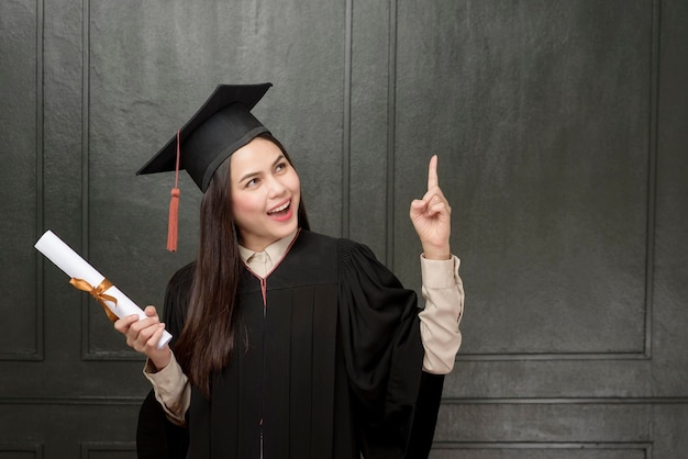 Portrait de jeune femme en robe de graduation souriant et acclamant sur fond noir