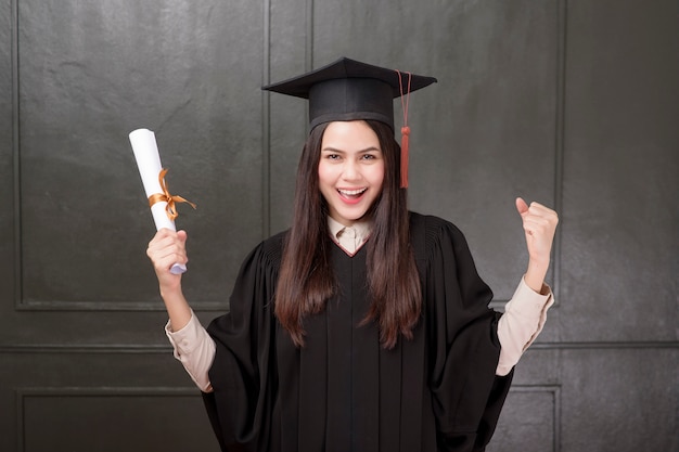 Portrait de jeune femme en robe de graduation souriant et applaudissant sur fond noir