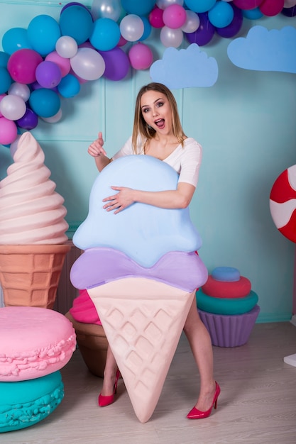 Portrait de jeune femme en robe rose tenant une grosse glace et posant sur fond décoré