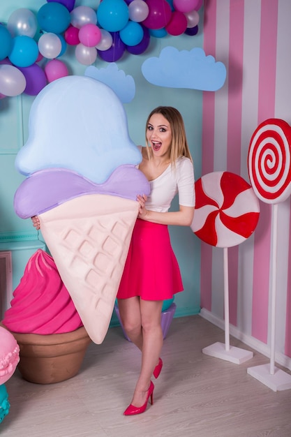 Portrait de jeune femme en robe rose tenant une grosse glace et posant sur fond décoré