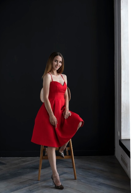 portrait d'une jeune femme en robe rouge assise sur un tabouret de bar haut