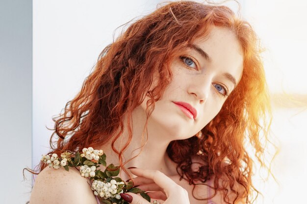 Portrait de jeune femme rousse magnifique près de la fenêtre avec une fleur, ambiance printanière